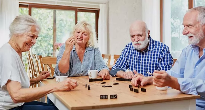 A group of seniors sits around a table playing dominoes, smiling and engaged during a Brain Games session at Senior Day KC.