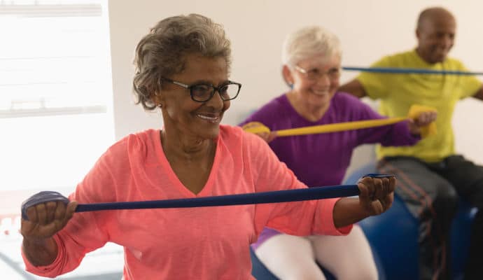 A group of older adults seated in chairs, smiling and lifting resistance bands together during a guided exercise session at Senior Day KC.